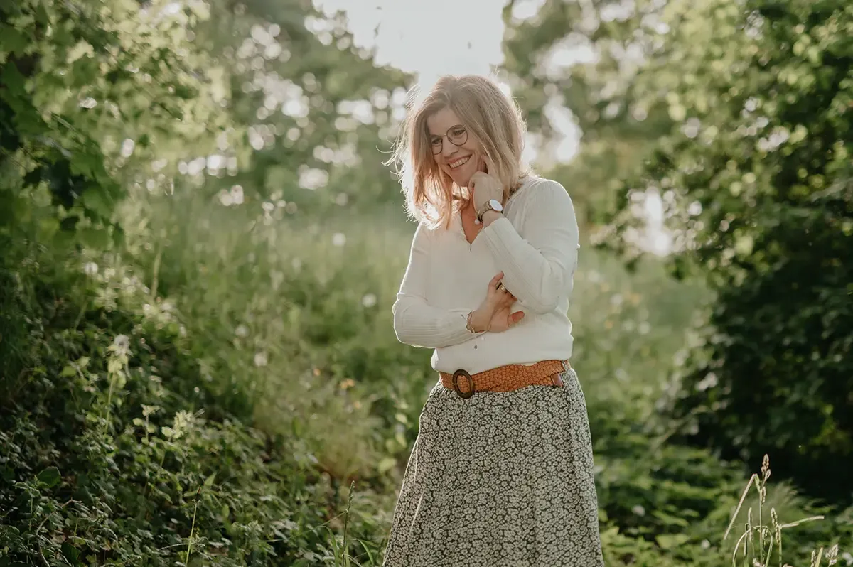 Kerstin steht in der Natur und sinniert lächelnd